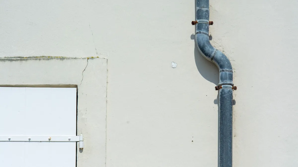 A downspout and its jointed elbows running down an exterior wall