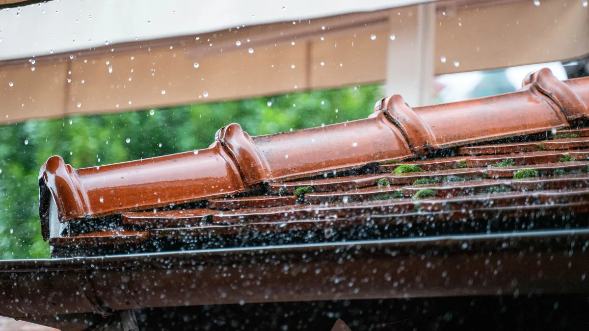 Heavy rain falling past the edge of a roof and its gutter